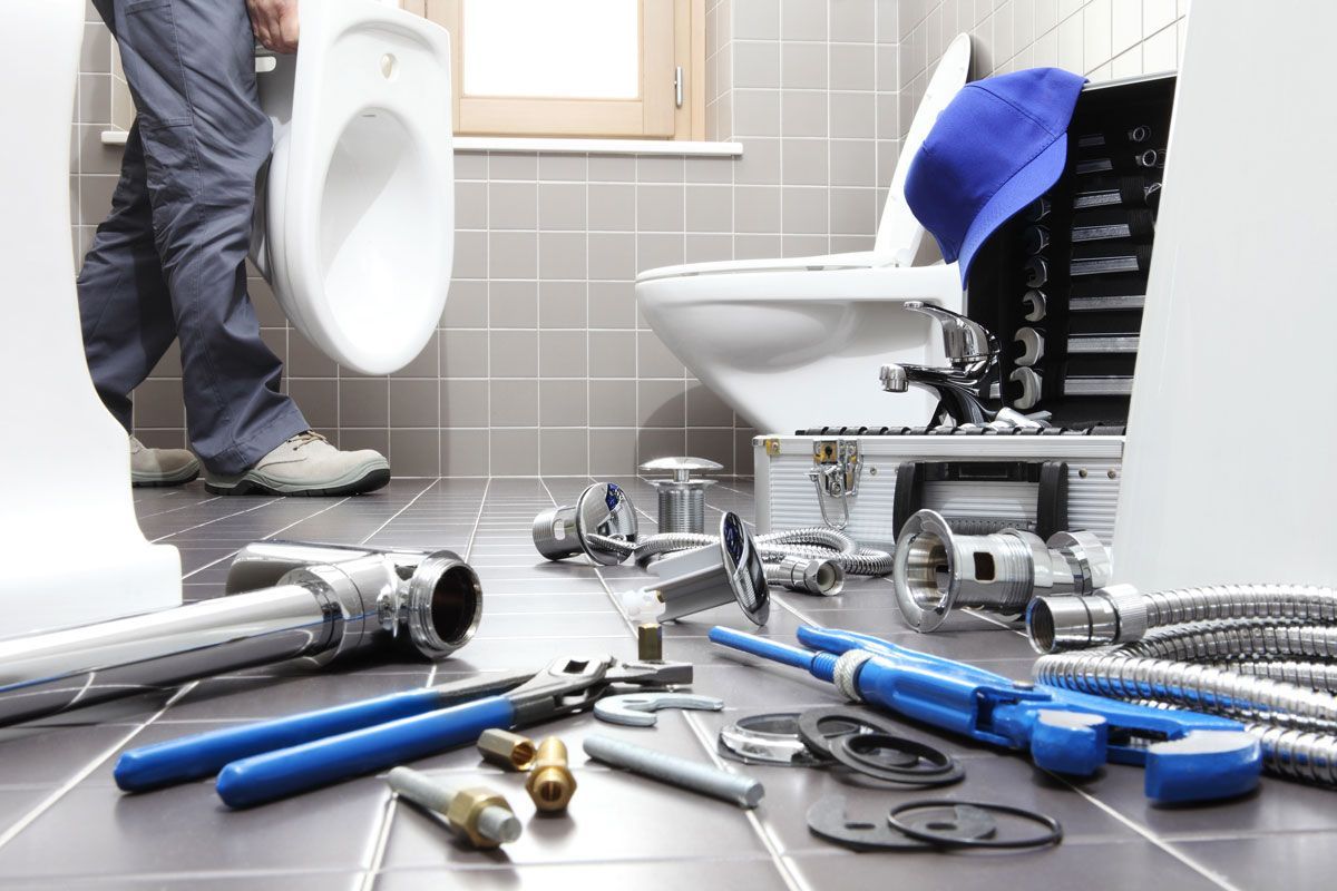 Plumber installing a toilet in a bathroom with tools scattered on the floor.
