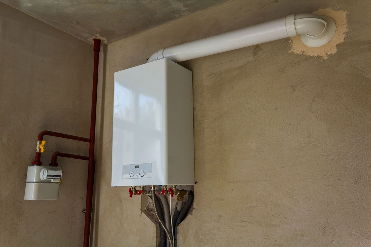 White wall-mounted gas boiler with connected pipes and vent in a corner. Brown gas pipe on the left.