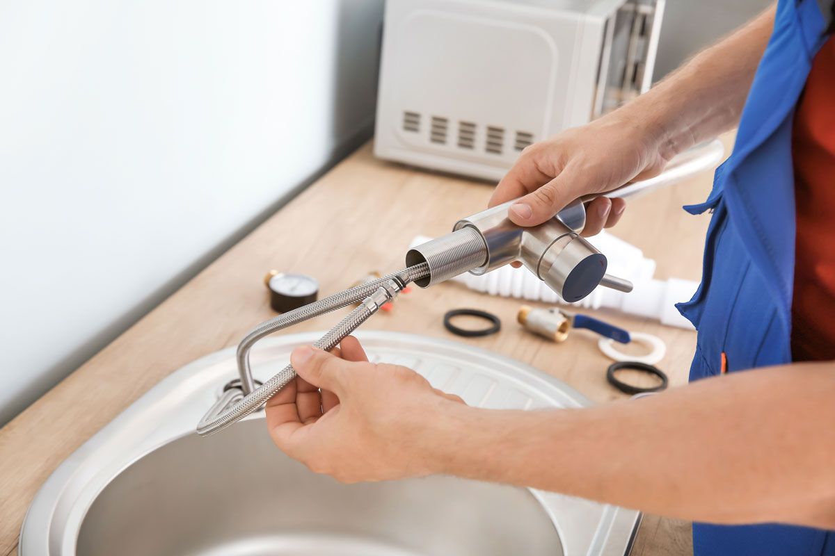 Plumber connecting faucet to sink with tools on counter.