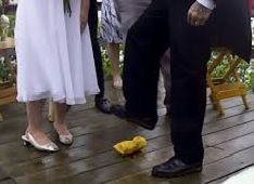 People standing on a wooden deck with a yellow bird on the floor between them