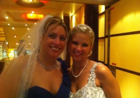 Two women smiling and posing in formal dresses in a warmly lit hallway