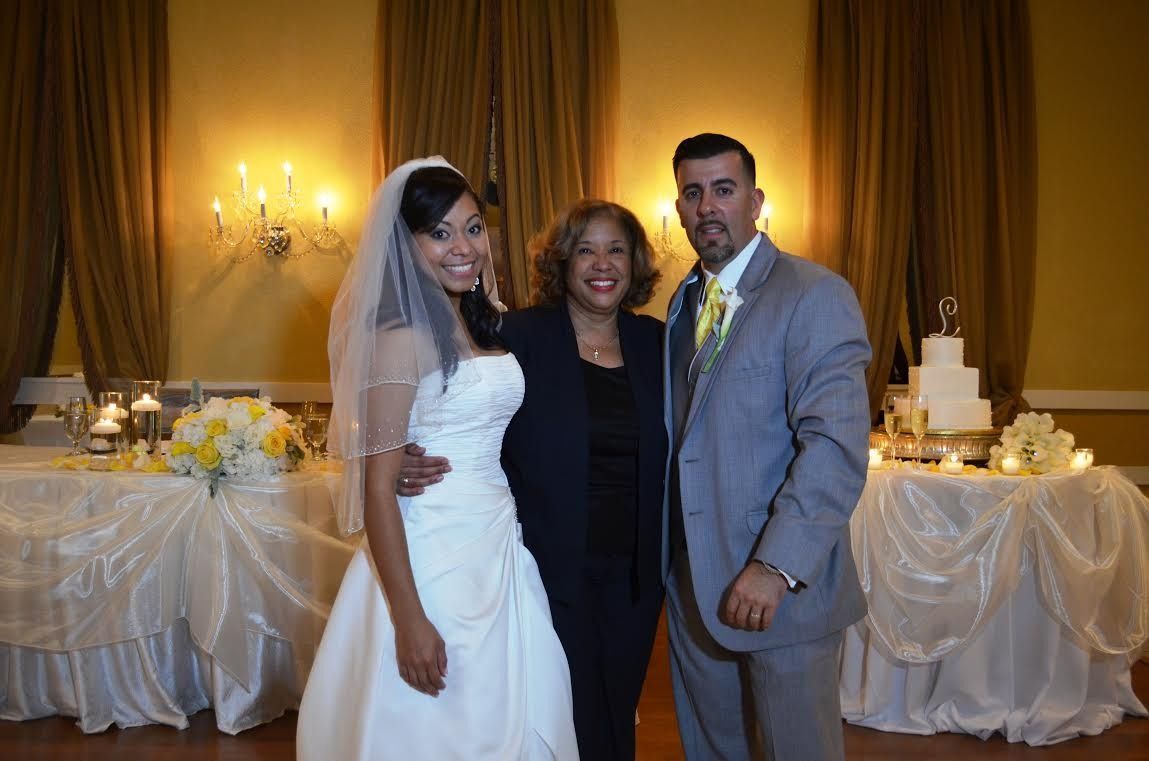 Bride and groom pose with a woman at a wedding reception table decorated with candles and drapes.