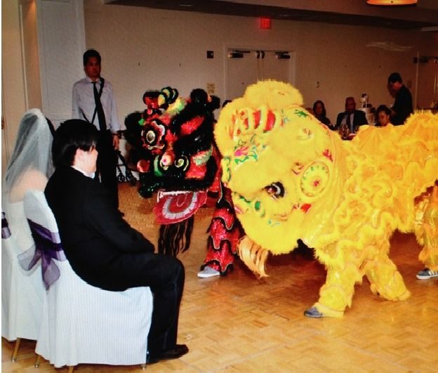 Colorful lion dance performers approach seated guests in a banquet hall, with a bright yellow lion in front.