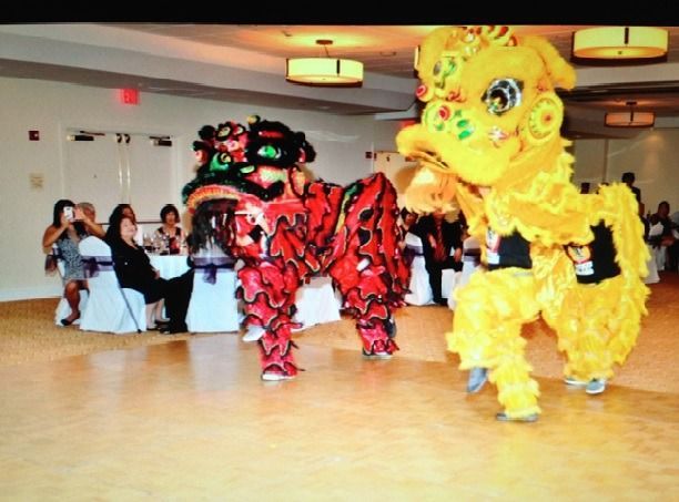 Two lion dancers in red and yellow costumes perform in a banquet hall for seated guests.