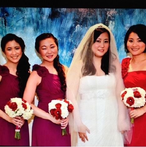 Bride in white veil stands with three bridesmaids holding red and white bouquets against a blue backdrop