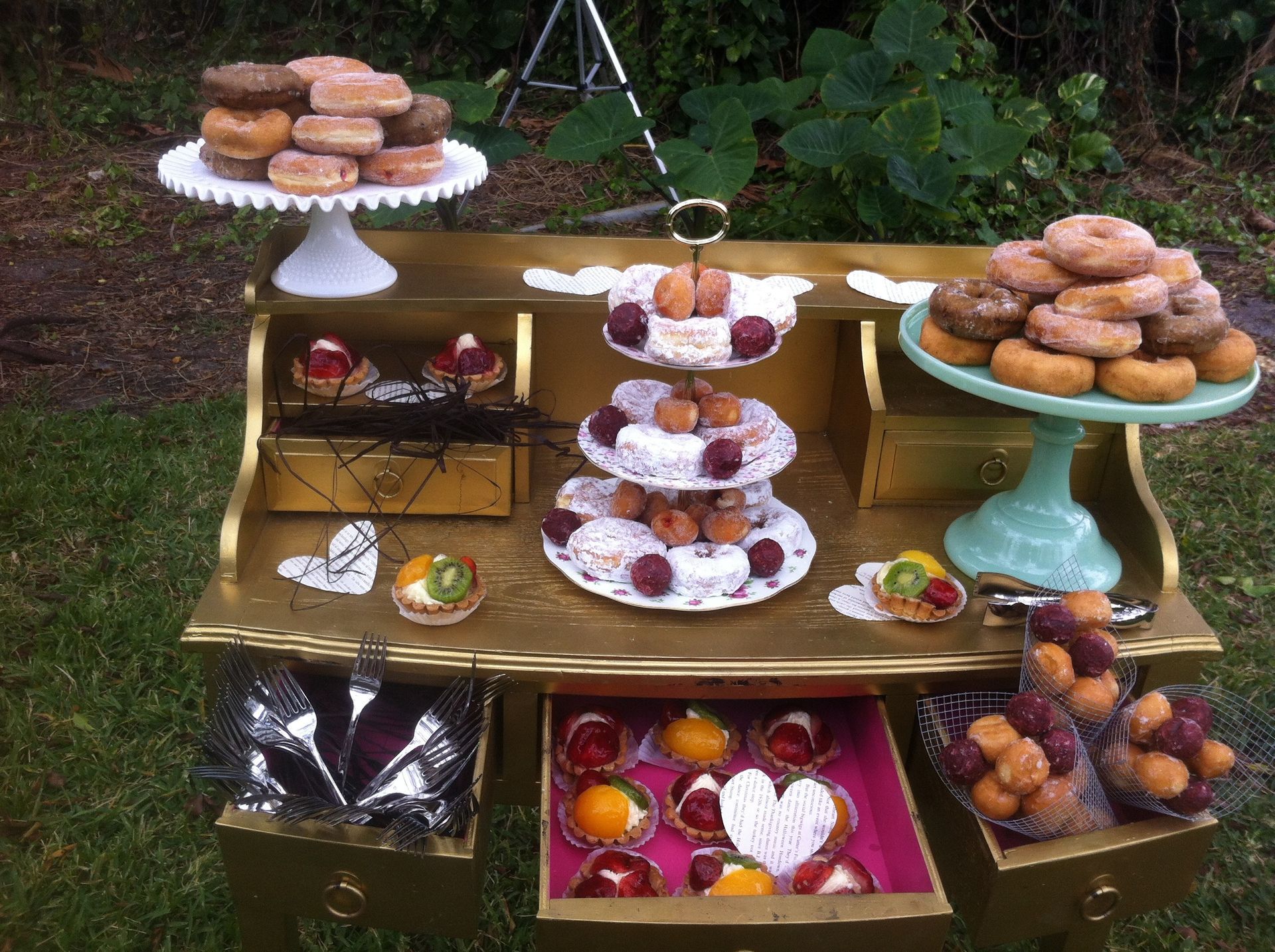 Tiered dessert display with assorted pastries, fruit, and chocolates on a gold table outdoors