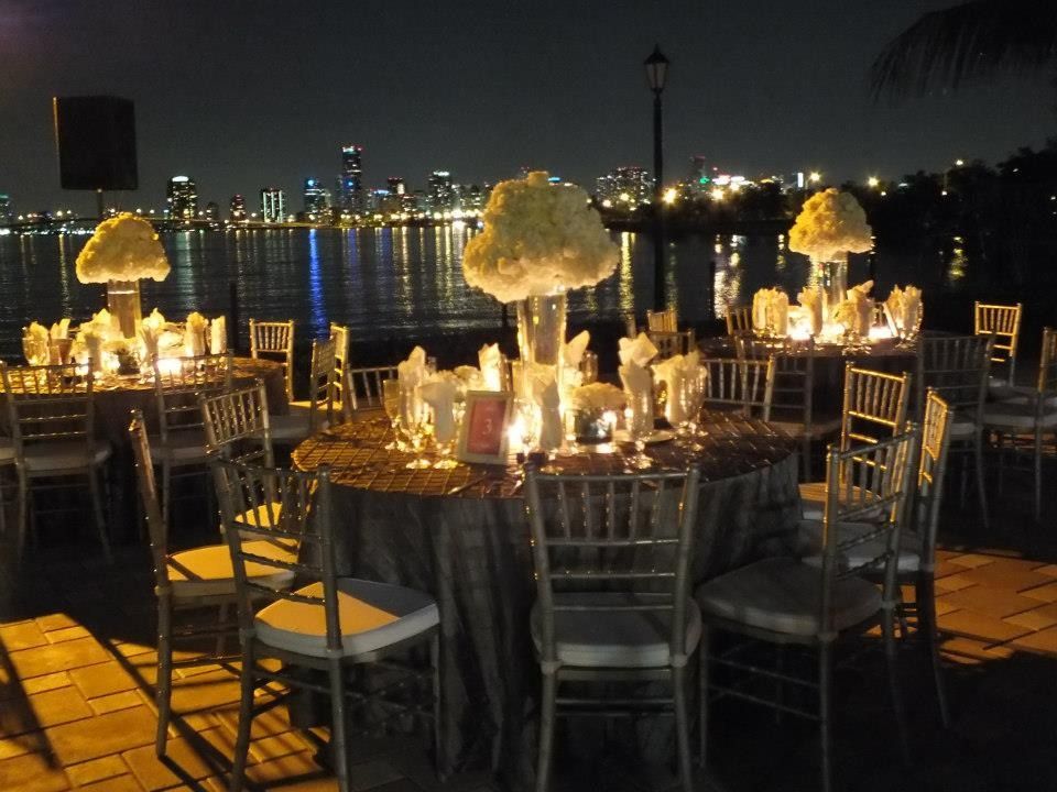 Elegant outdoor dining table lit by candles and floral centerpieces, overlooking a city skyline at night