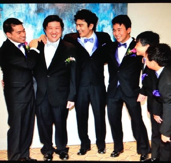 Five men in black suits and purple bow ties smiling together at a formal event
