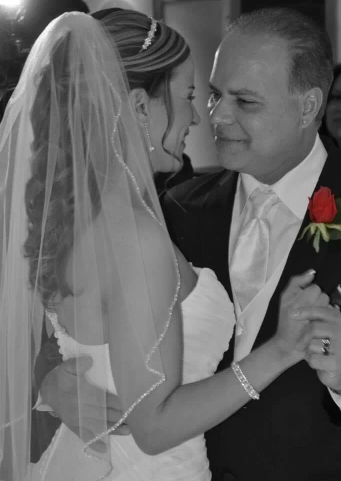 Bride and groom dancing closely at a wedding, smiling in black and white with a red rose boutonniere