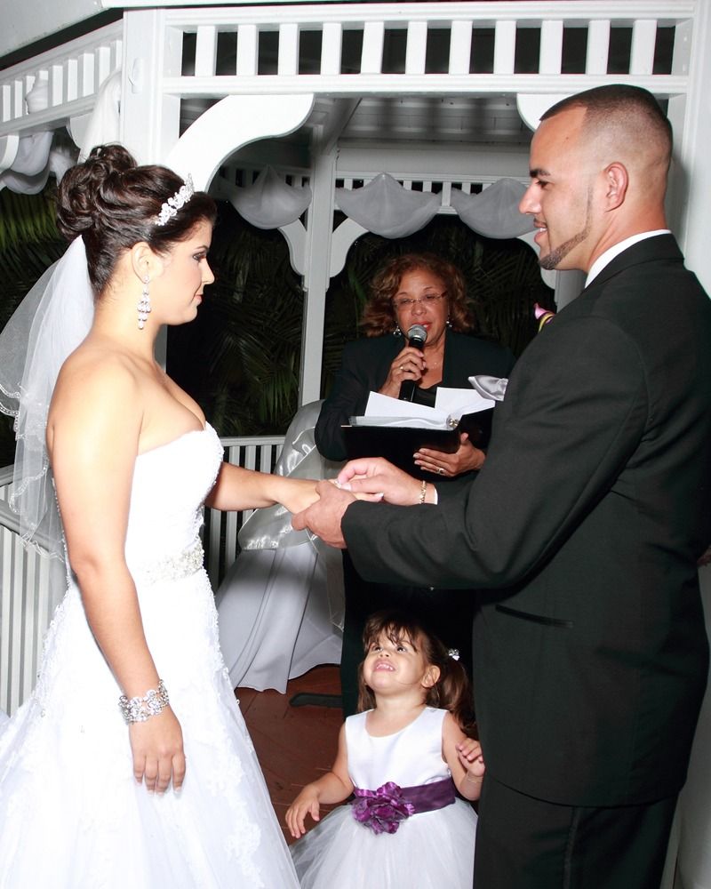 Bride and groom exchanging vows at an outdoor wedding ceremony with officiant and young flower girl