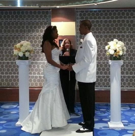 Wedding couple holding hands at an indoor ceremony with white floral pedestals and an officiant behind them