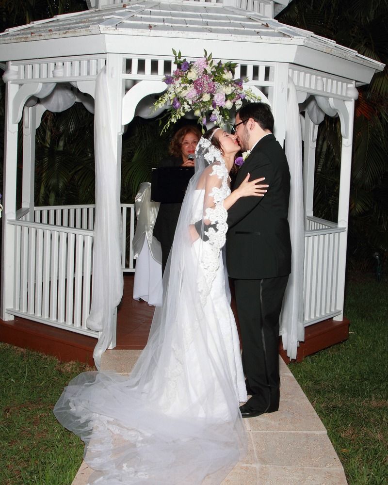 Bride and groom kissing at a white gazebo wedding ceremony with a floral arrangement