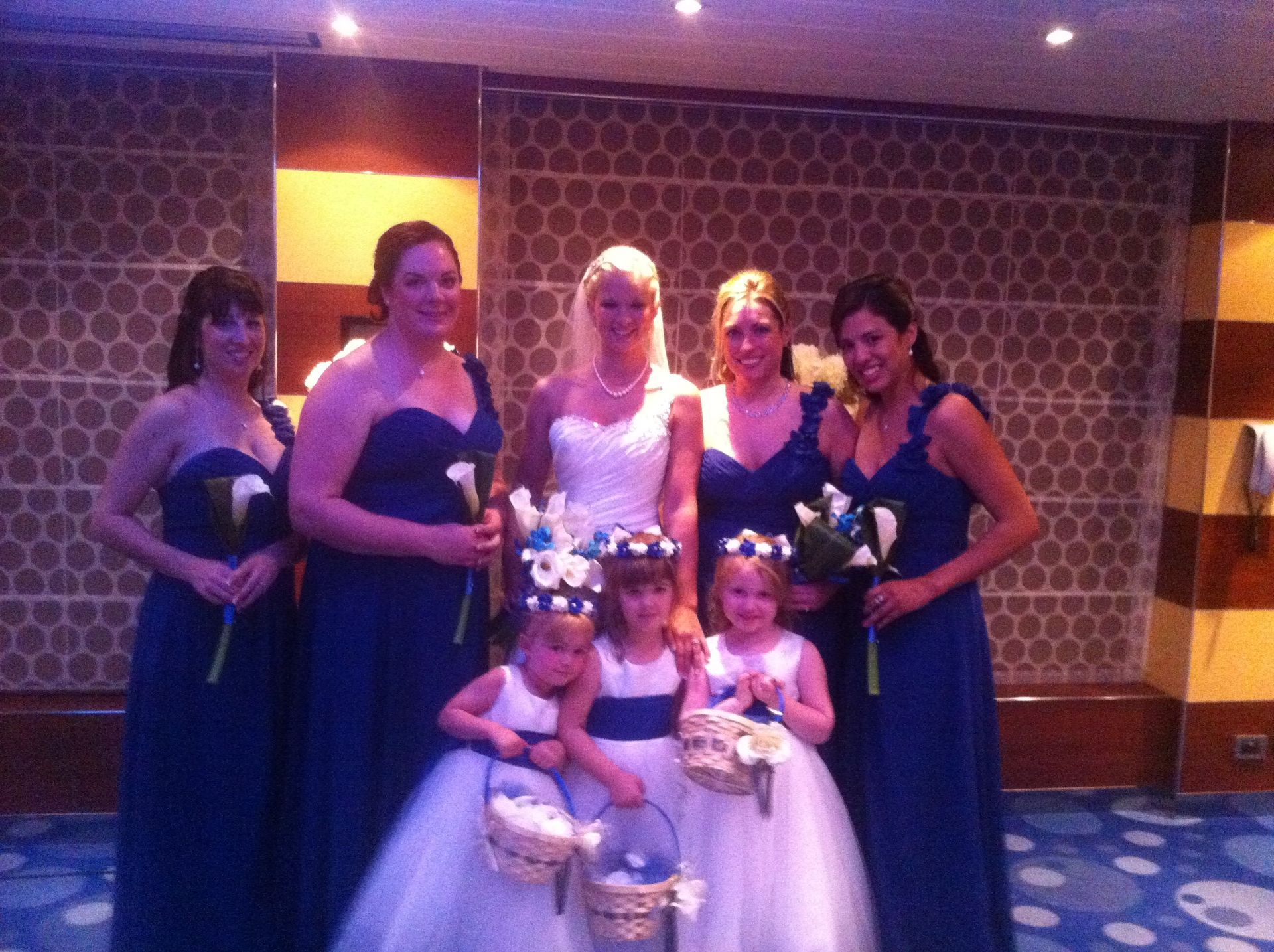 Formal group posed indoors, with five adults and two children in dresses holding bouquets.