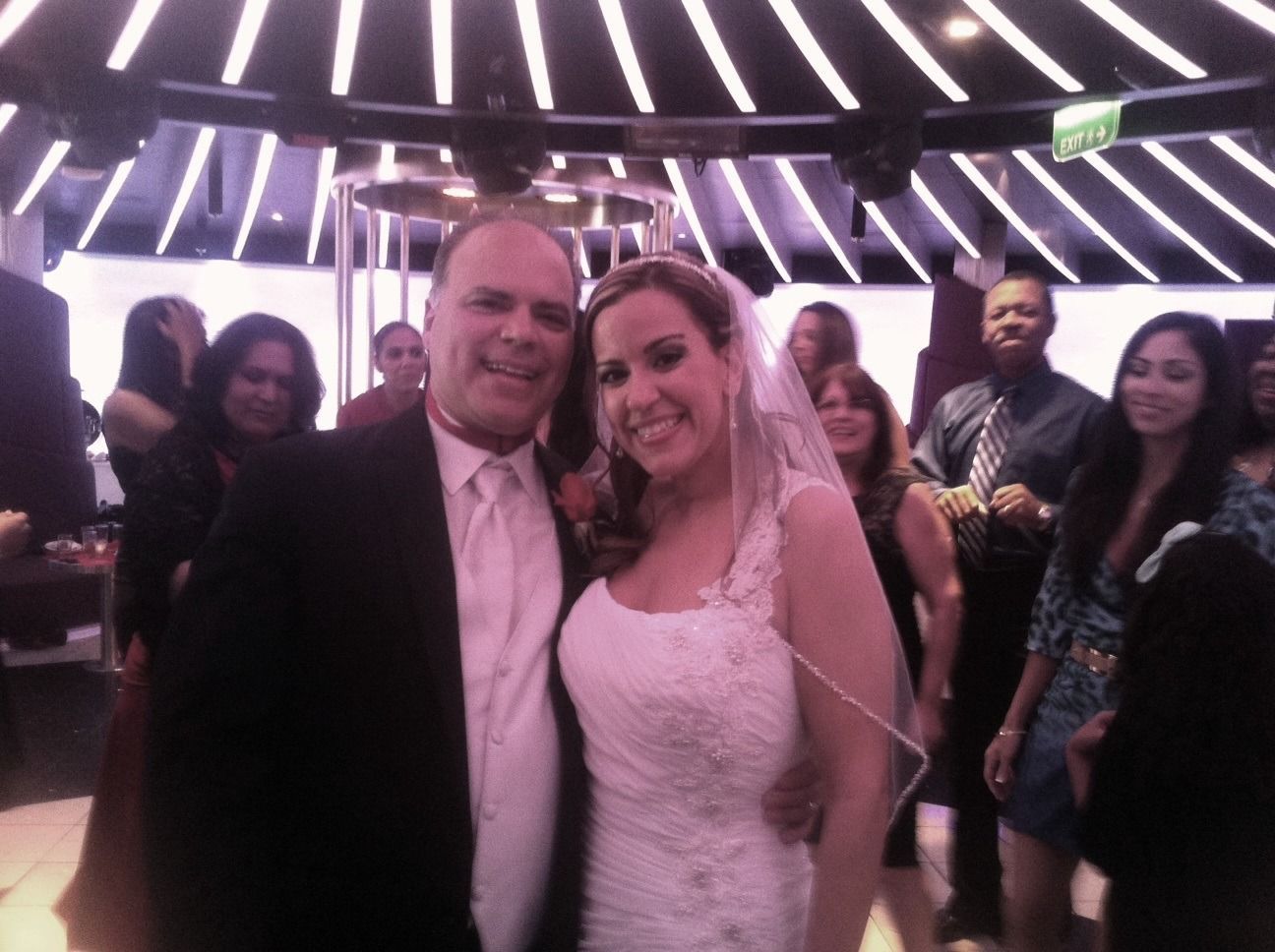 Couple smiling in formal attire at a lively party under purple lighting