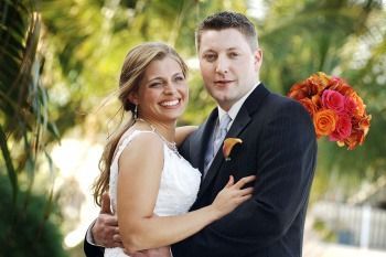 Smiling couple in wedding attire posing outdoors with orange flowers behind them