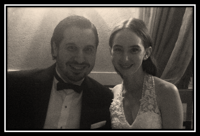 Two people in formal wear smiling for a black-and-white selfie indoors