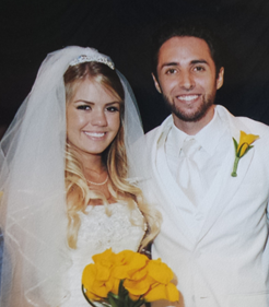 Wedding couple in white attire, smiling and holding a bouquet of yellow flowers.