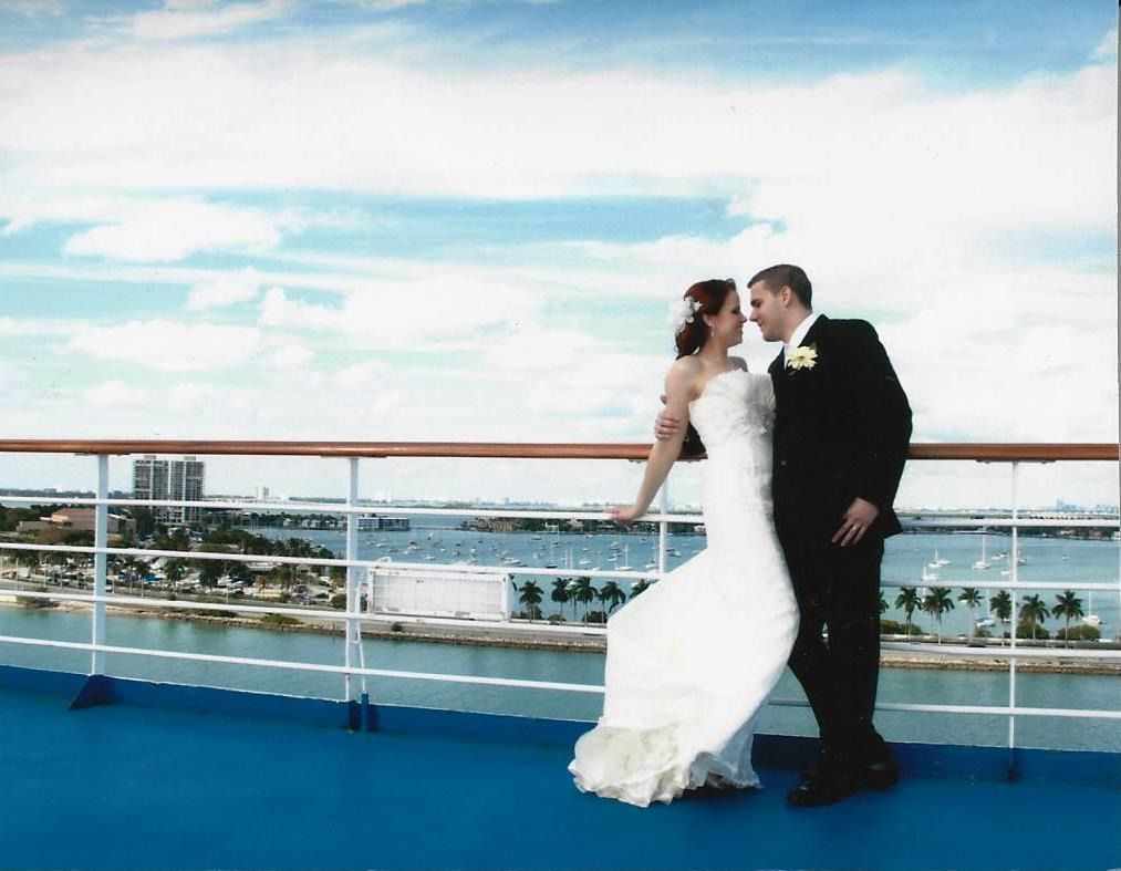 Bride and groom embracing on a ship deck with ocean and city skyline in the background