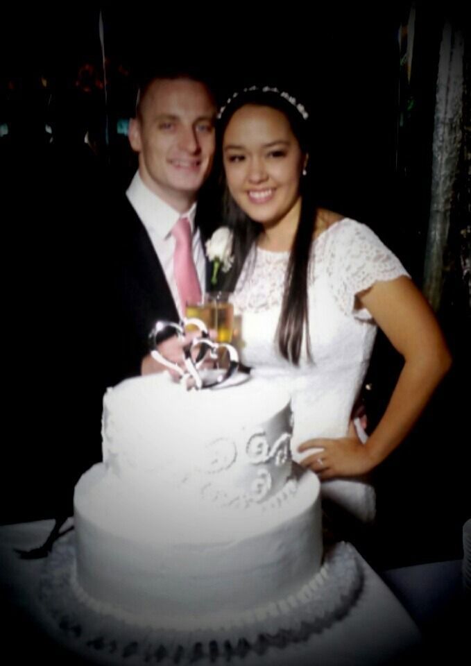 Couple posing behind a white decorated cake with a pink topper at a celebration