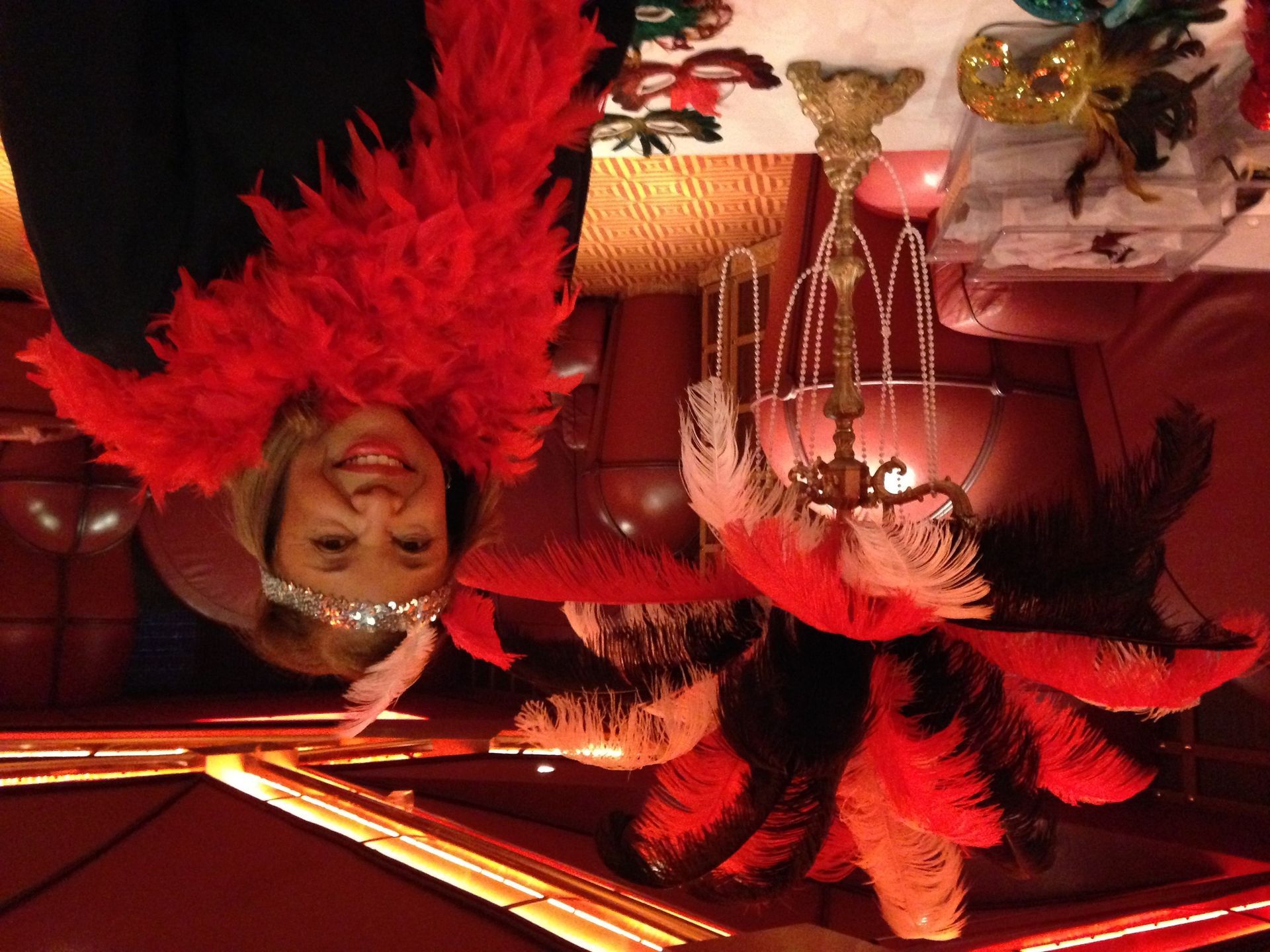 Two people in red feather boas performing on a warm-lit stage with chandeliers and draped curtains