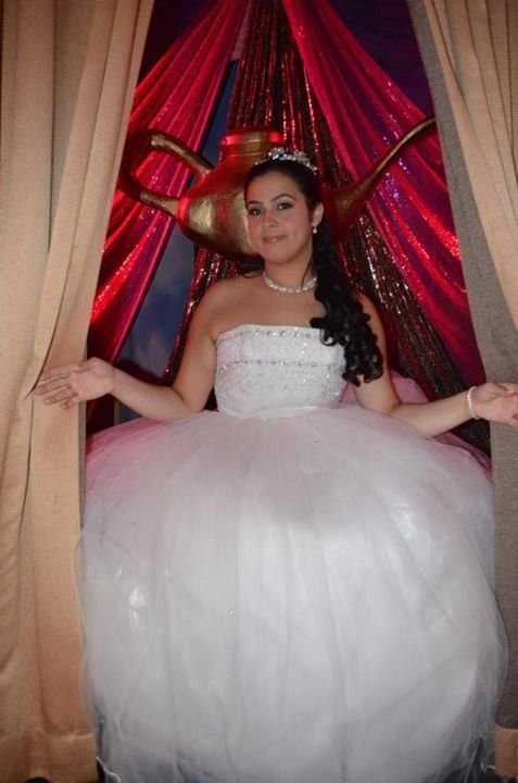 Woman in a white ball gown posing in front of red curtains and gold drapes