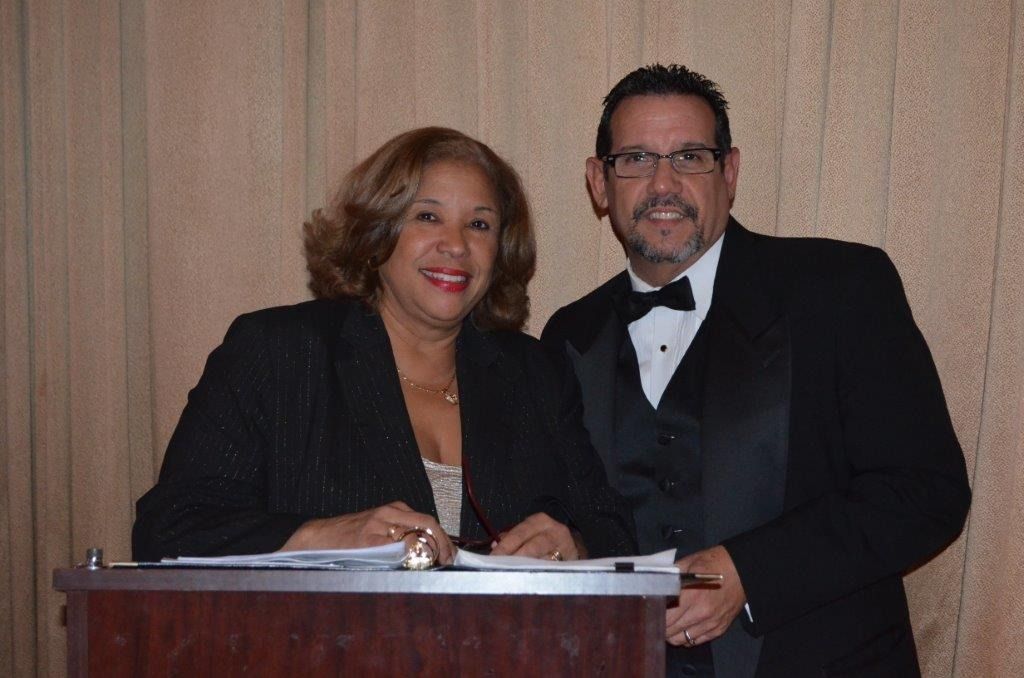 Two formally dressed people standing behind a podium, smiling at an event