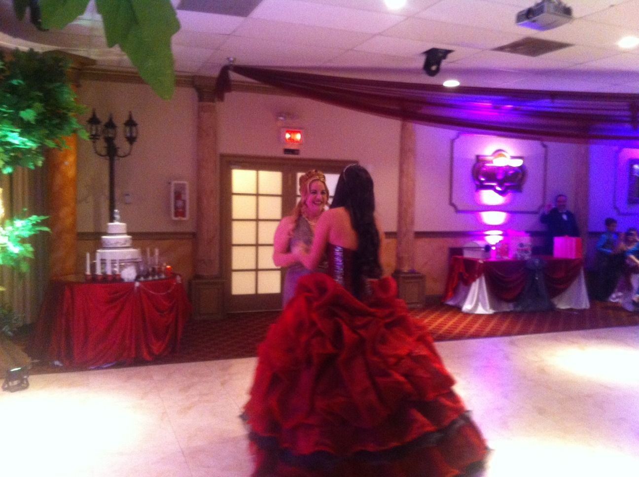 Two women dancing in a ballroom reception hall with purple lighting and red table decorations