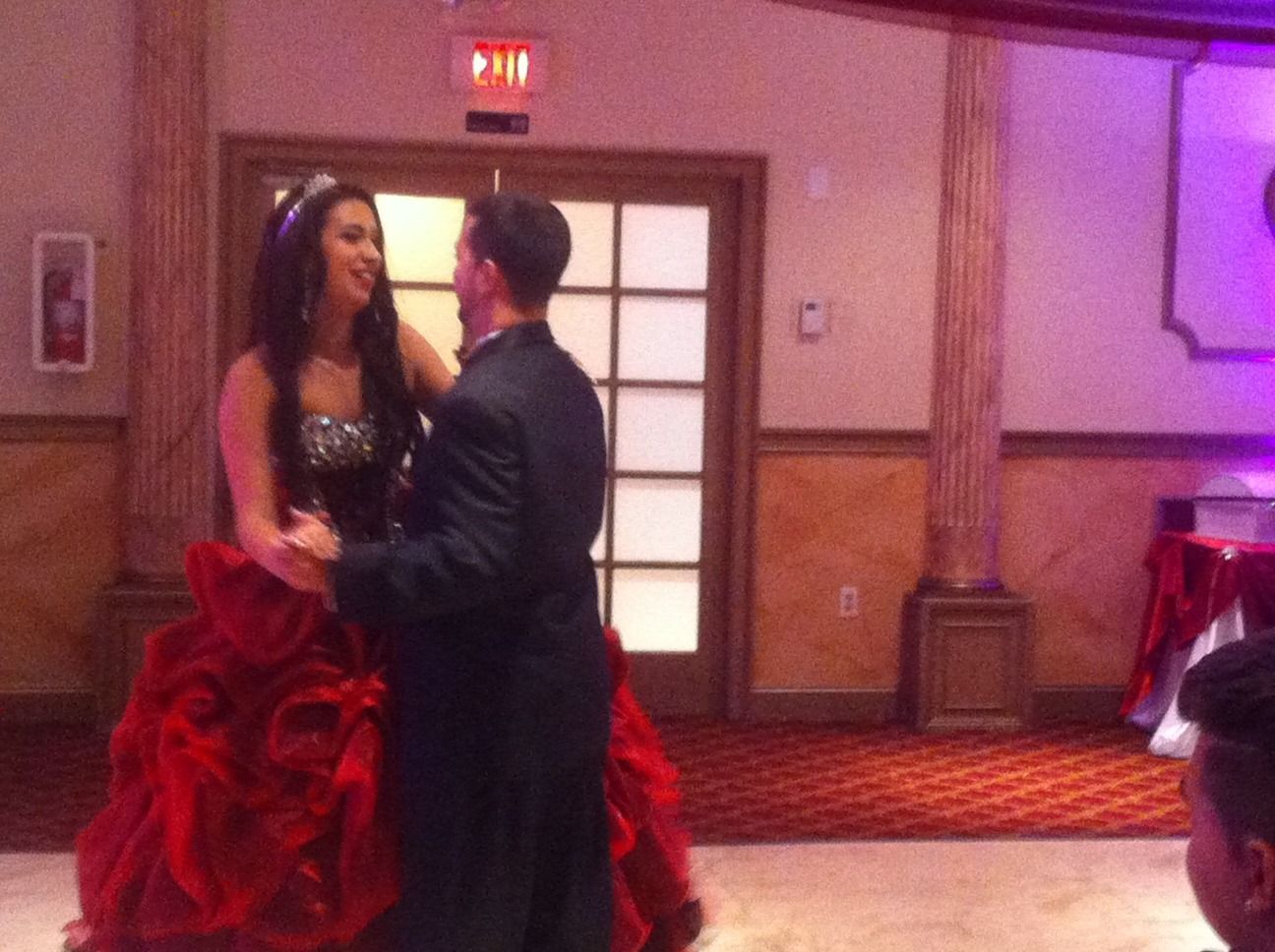 Couple dancing in a formal banquet hall, woman in a red ruffled gown and man in a dark suit.