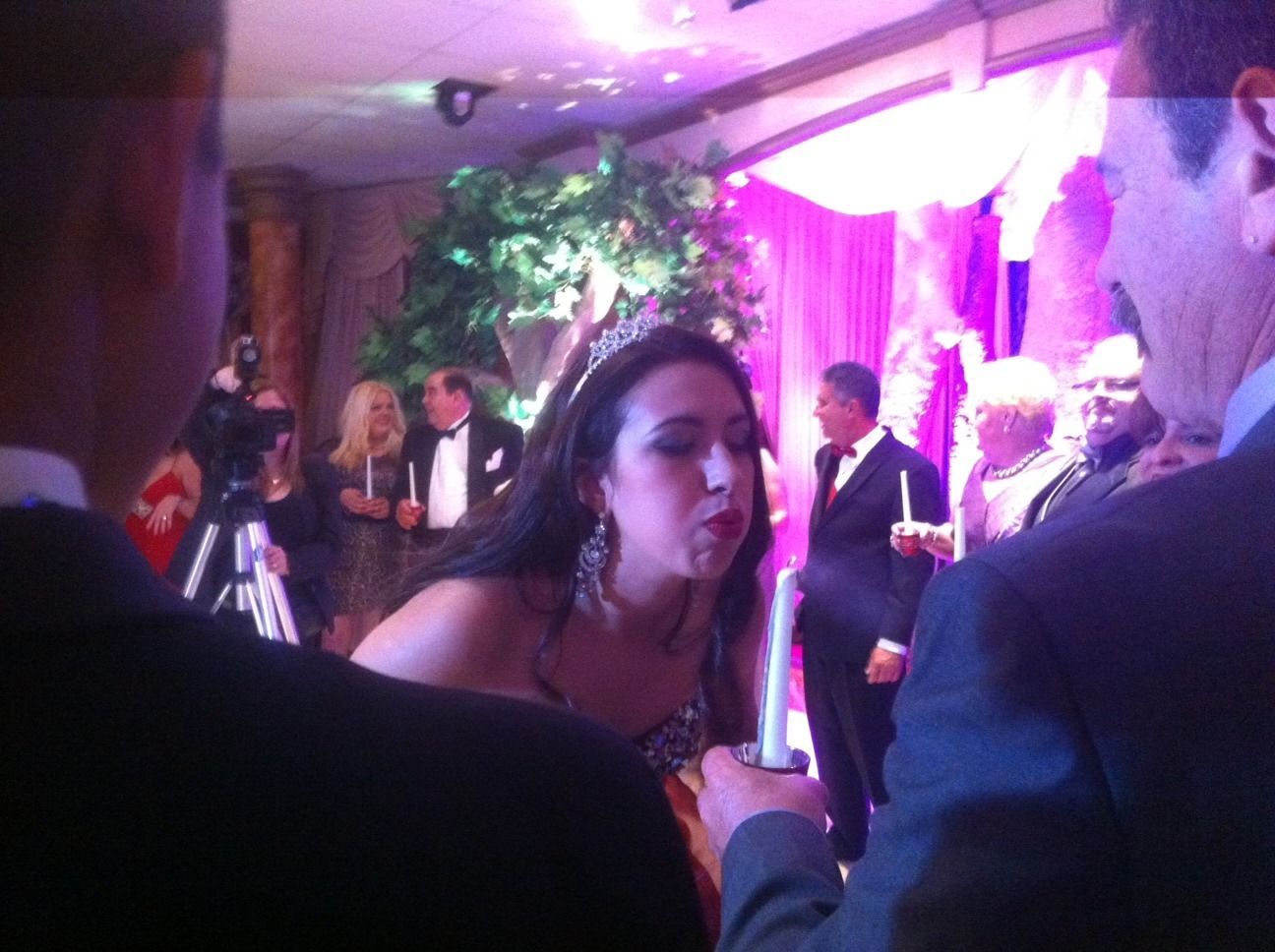 Woman leaning toward a microphone at a purple-lit indoor event with people in the background
