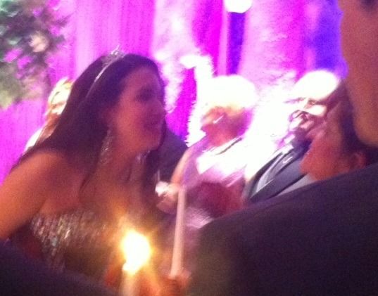 People socializing at a purple-lit event, with a woman holding a lit candle in the foreground