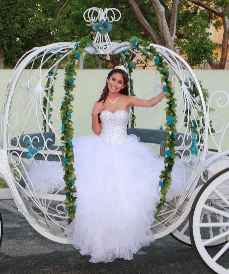 Woman in a white gown posing in a decorative white carriage with floral accents outdoors
