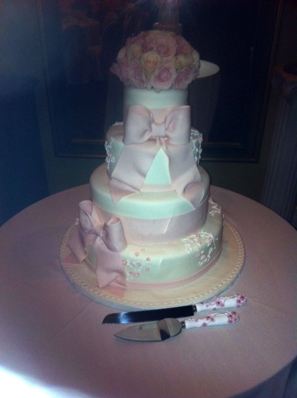 Three-tier pink and white cake with flowers, centered on a round table with a cake knife and serving server.