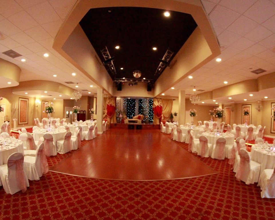 Elegant banquet hall with round tables, white chair covers, and a polished wooden dance floor