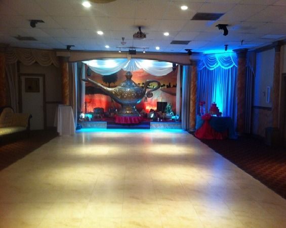 Decorated ballroom with a lit stage and dance floor, blue and warm lighting, and draped curtains.