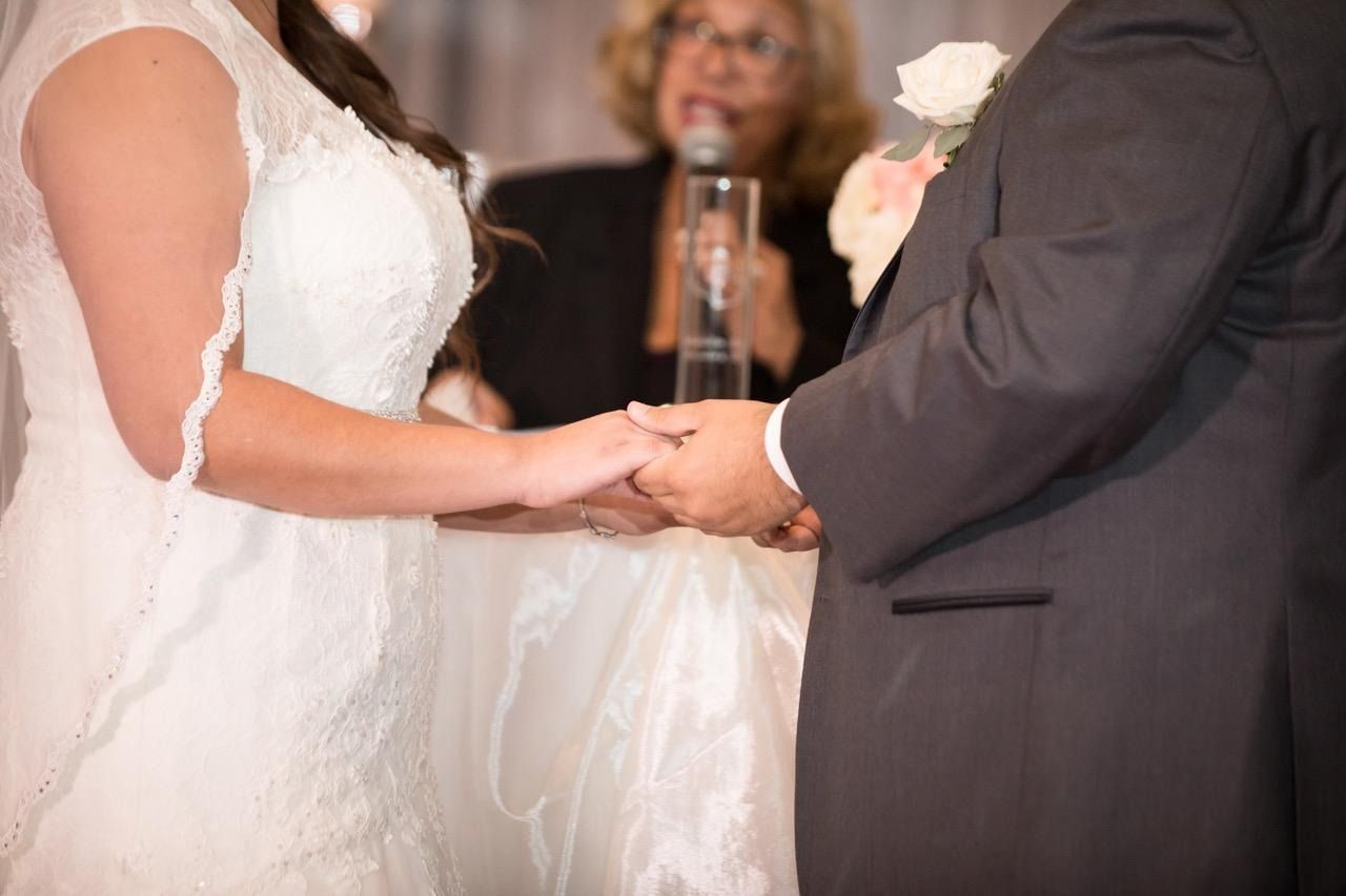 Bride and groom holding hands during their wedding ceremony, with officiant in the background
