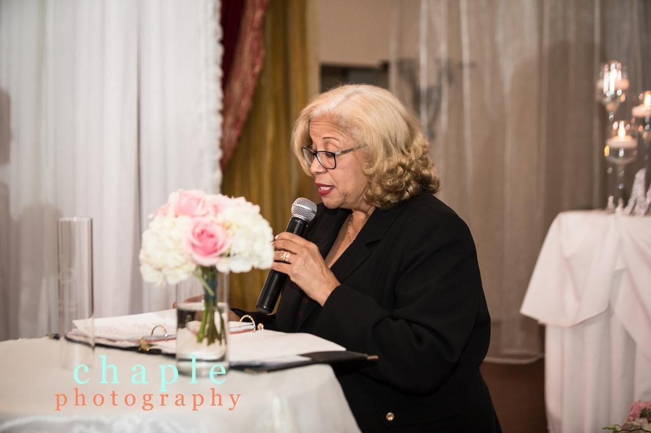 Woman speaking into a microphone at a table with flowers during an indoor event