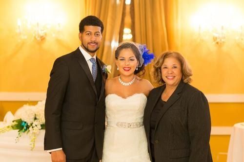 Three people posing together at a wedding reception, with the bride in a white gown between two guests.