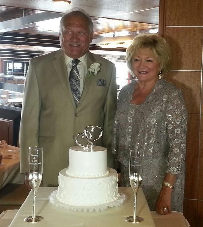 Couple standing beside a white tiered cake with champagne flutes at a formal celebration