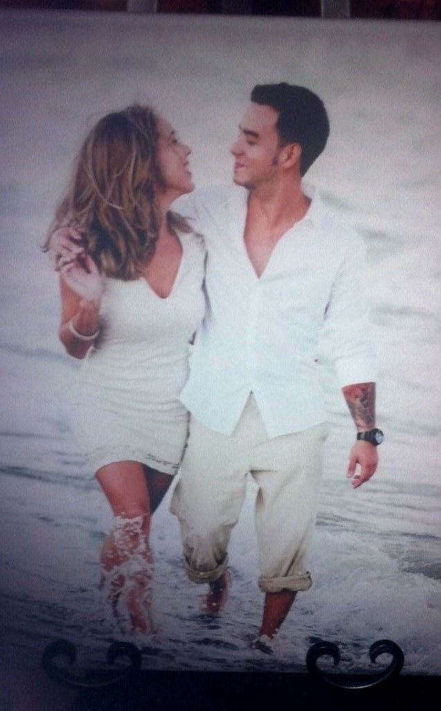 Couple in white clothes walking on the beach, looking at each other and smiling.