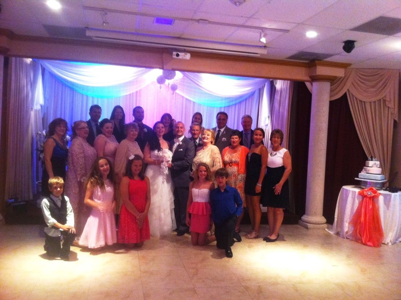 Group posing for a formal event in a decorated banquet hall with draped curtains and colorful lighting