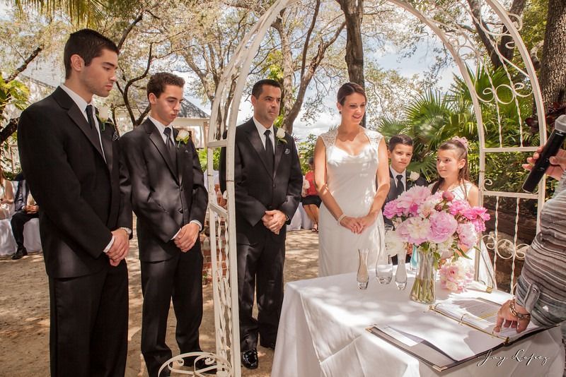 Wedding couple and guests standing beside a decorated signing table with pink flowers outdoors