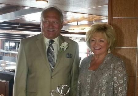 Two smiling people posing indoors, one holding a trophy, in a wood-paneled room