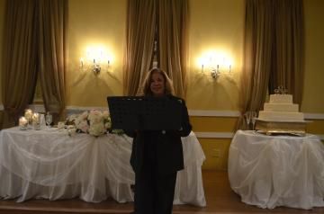 Woman speaking at a podium in a gold-lit banquet hall, with decorated tables and a tiered cake behind her