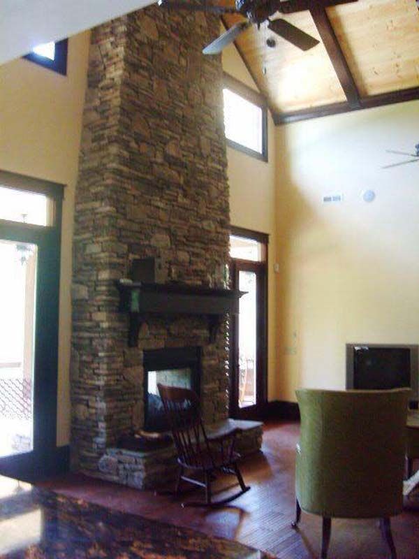 Stone fireplace in a living room, with a high ceiling, dark wooden beams and hardwood floor.