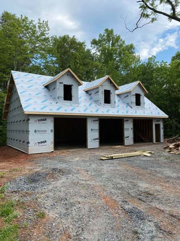 A partially built garage with three bays and three dormers, covered in Tyvek, set on gravel.