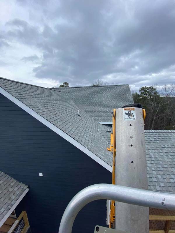 Blue-sided house with gray shingled roof under a cloudy sky, seen from a lift.