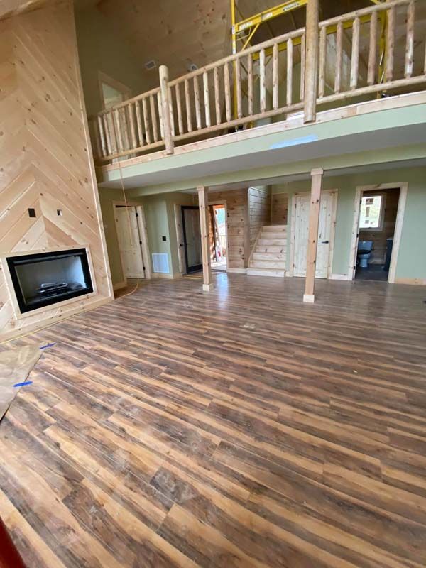 Spacious interior with wood floors, fireplace, and second-story balcony. Wooden beams and railing.