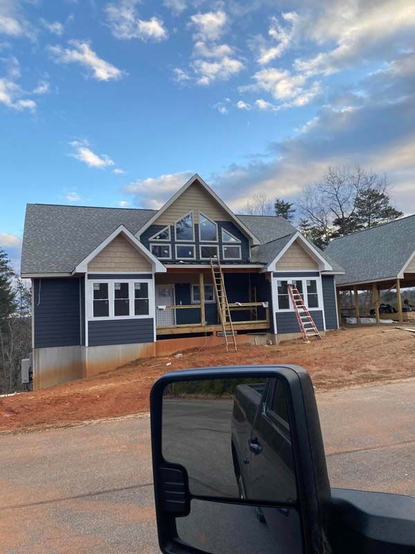 Newly constructed blue house with light-brown accents, many windows, and a partially finished porch.