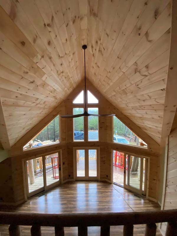 Interior view of a wooden-paneled room with large windows, a ceiling fan, and hardwood floors.