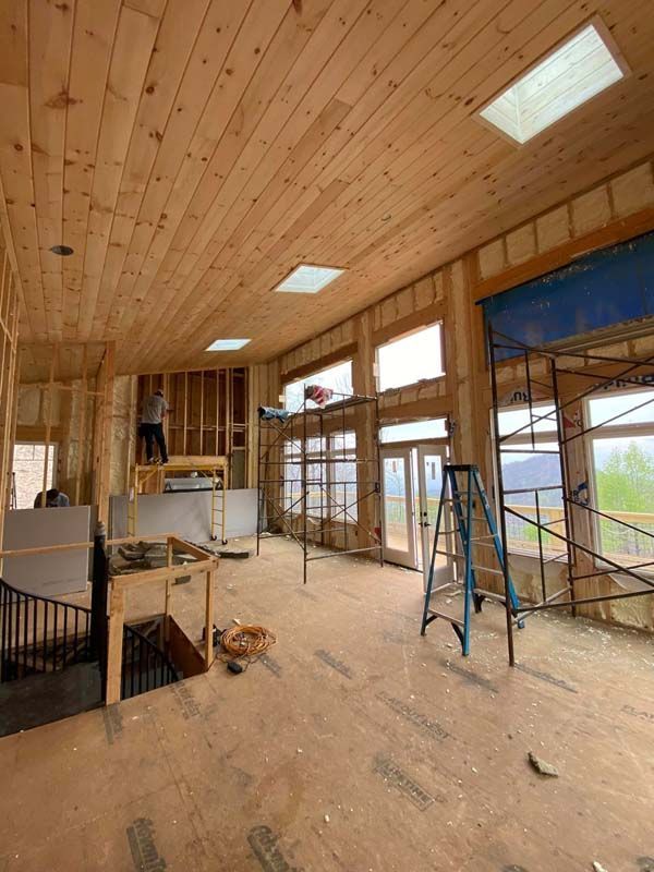Interior of a house under construction; wood ceiling and framing, windows, scaffolding, worker on a lift.